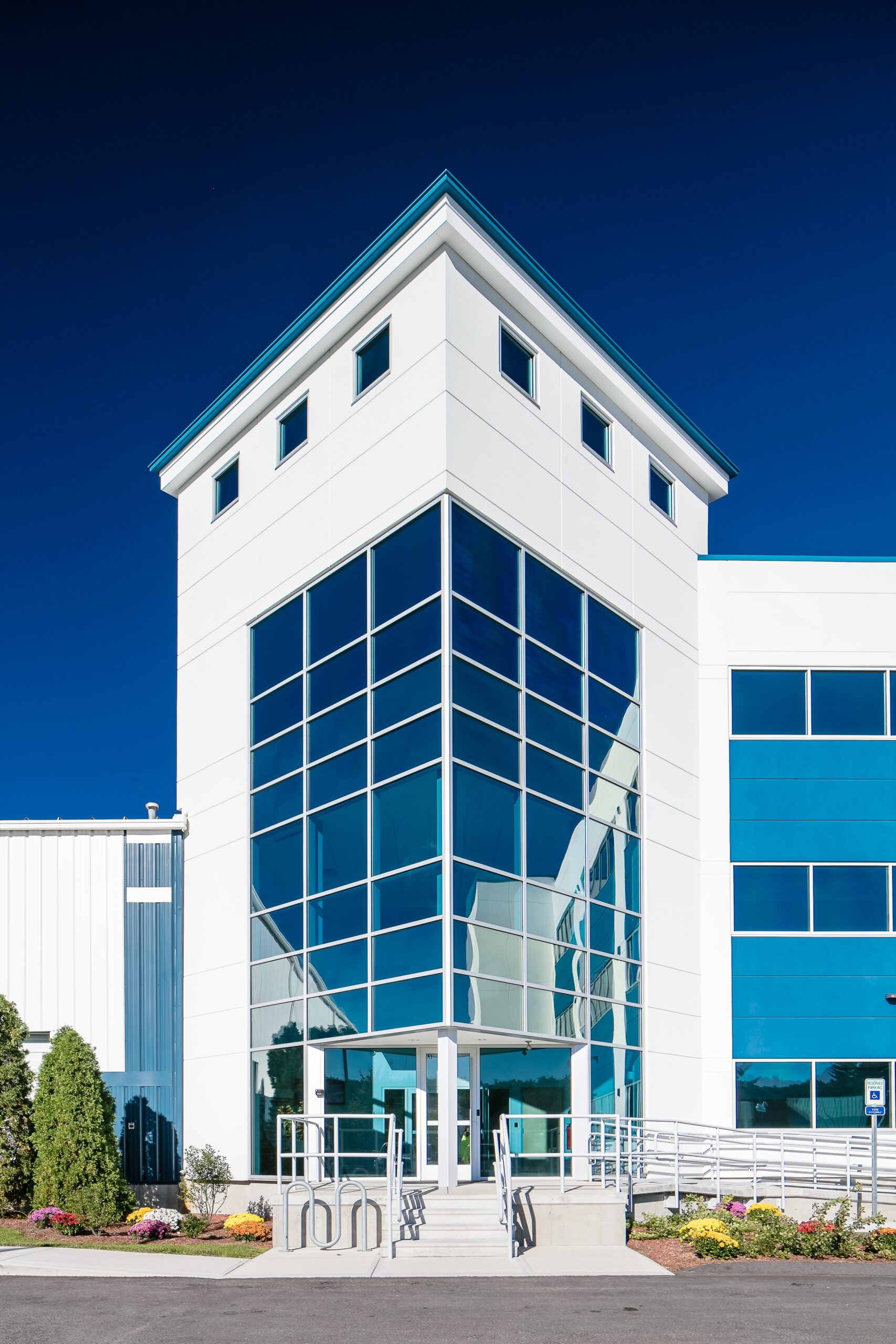 Modern commercial building with white metal panel exterior and large glass curtain wall entry tower.